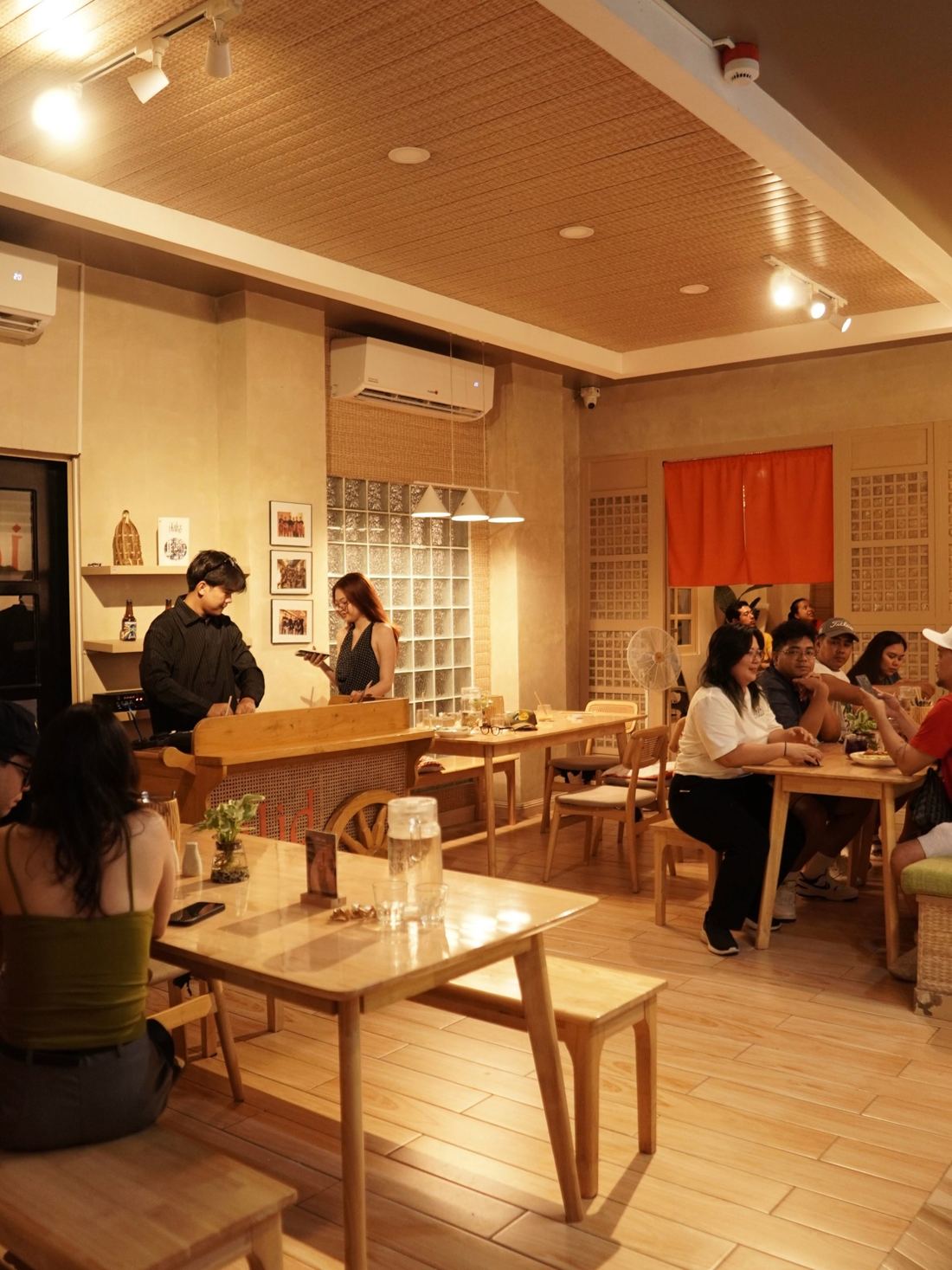 Silid's main dining room with wooden tables, glass-block wall and the Kape Kariton by the counter, full of guests