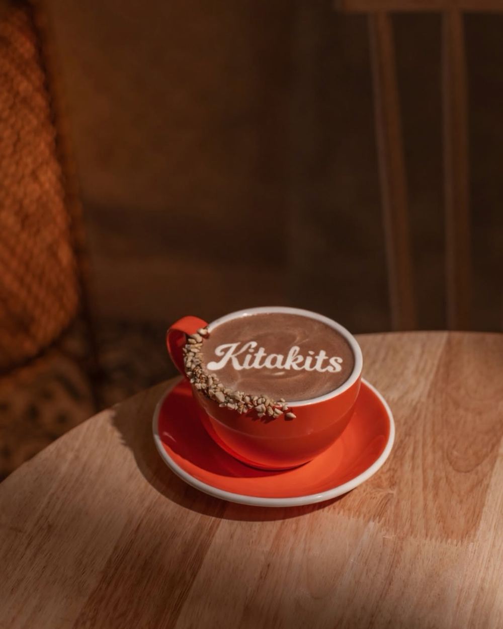 A red cup of tsokolate with 'Kitakits' latte art and a crushed-peanut rim