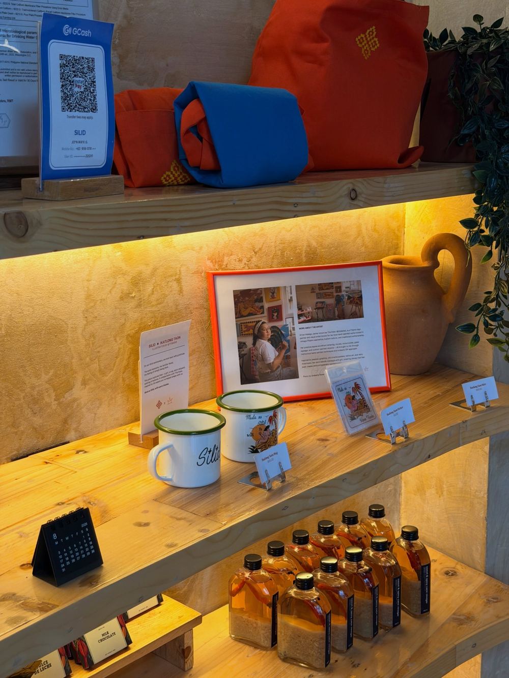 Silid merch shelf with enamel mugs, tote bags and bottled spiced vinegar
